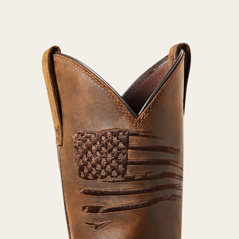 A brown work boot with an embossed American flag design on the upper part, featuring a square toe and a heel stabilizer.